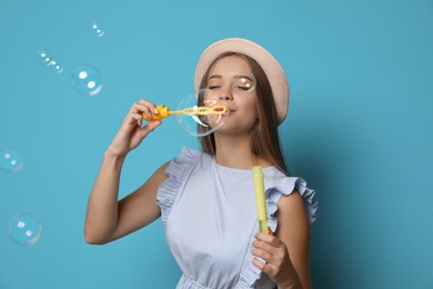 Young woman blowing soap bubbles on color background