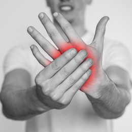 Man suffering from rheumatism on light background, closeup. Black and white effect with red accent in painful area