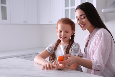 Photo of Happy girls with fresh ripe tangerine at table in kitchen