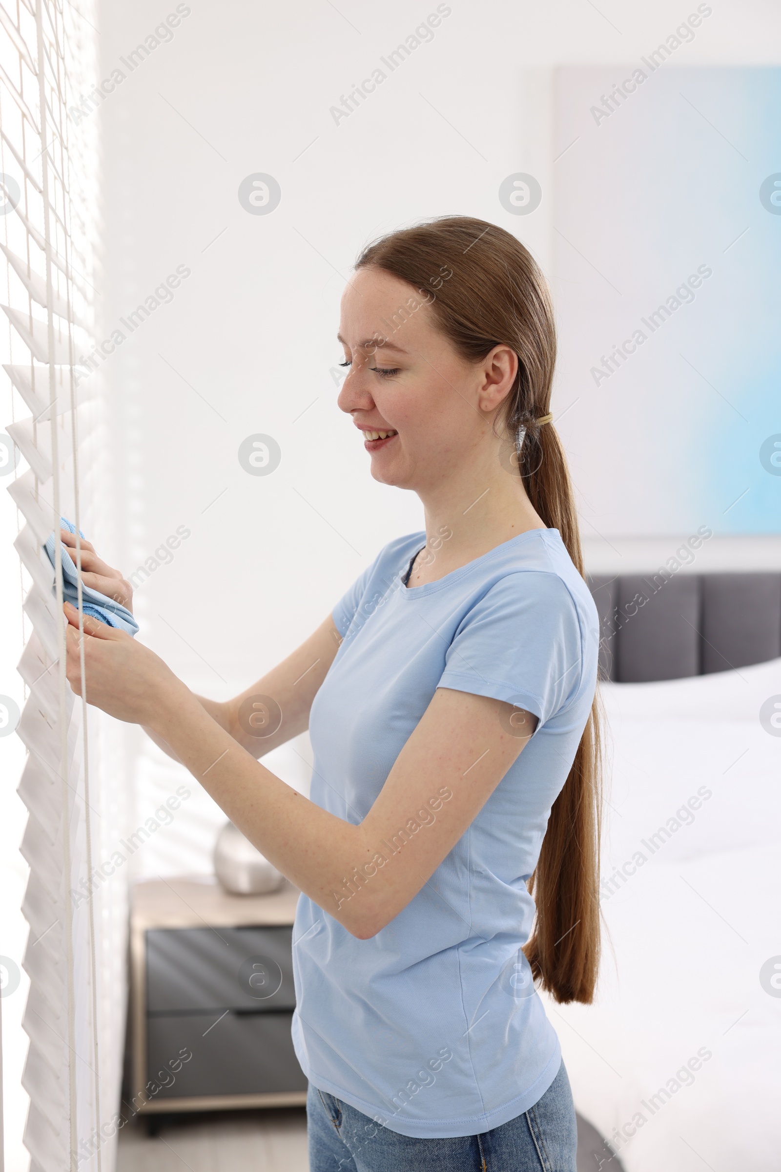 Photo of Woman with microfiber cloth wiping blinds at home