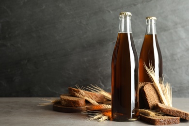 Photo of Bottle of delicious fresh kvass, spikelets and bread on grey table. Space for text