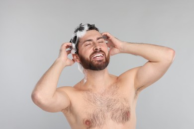 Photo of Happy man washing his hair with shampoo on grey background