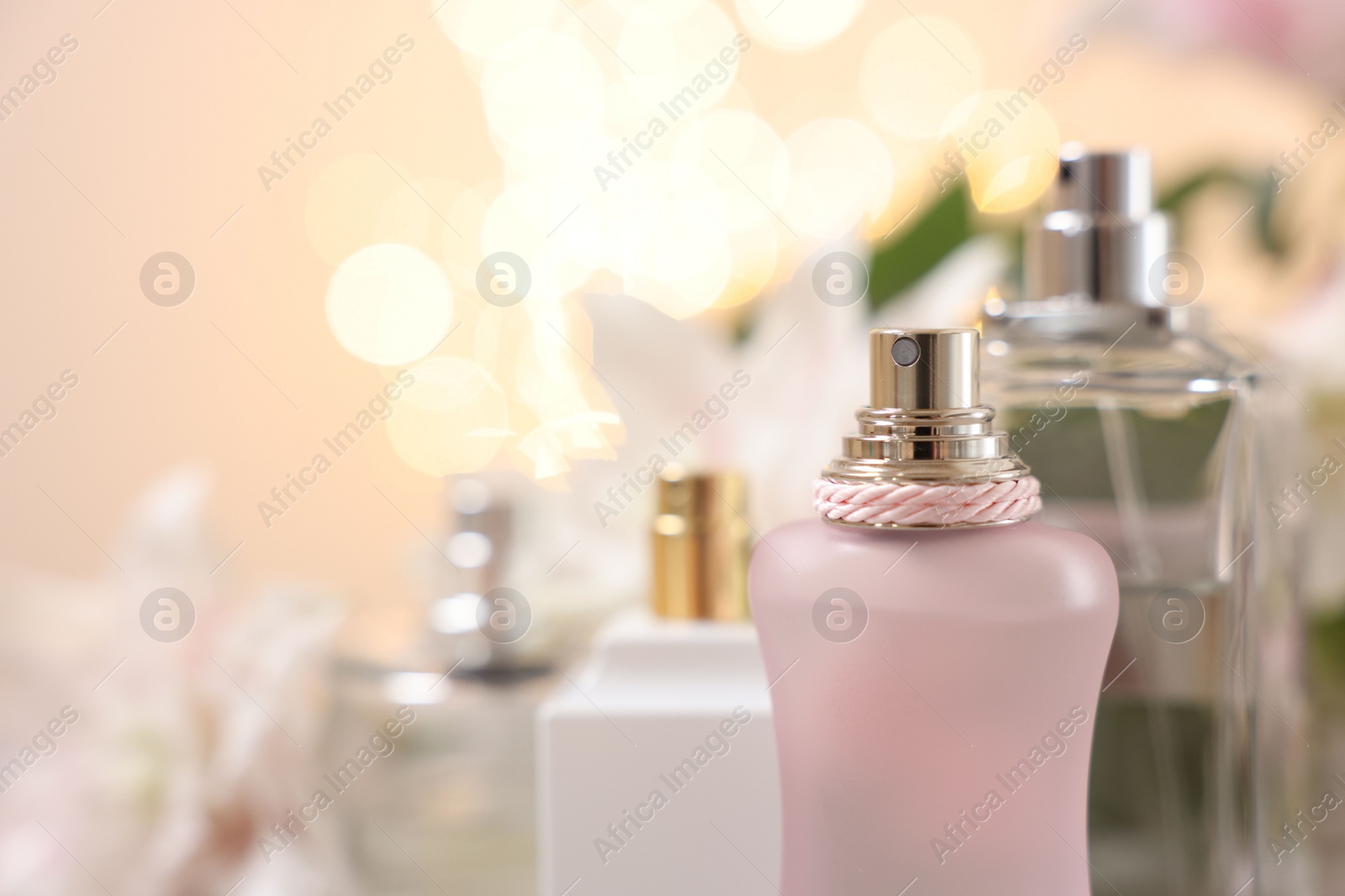 Photo of Bottles of perfume against beautiful lily flowers and blurred lights, closeup. Space for text