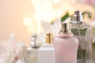 Bottles of perfume against beautiful lily flowers and blurred lights, closeup. Space for text