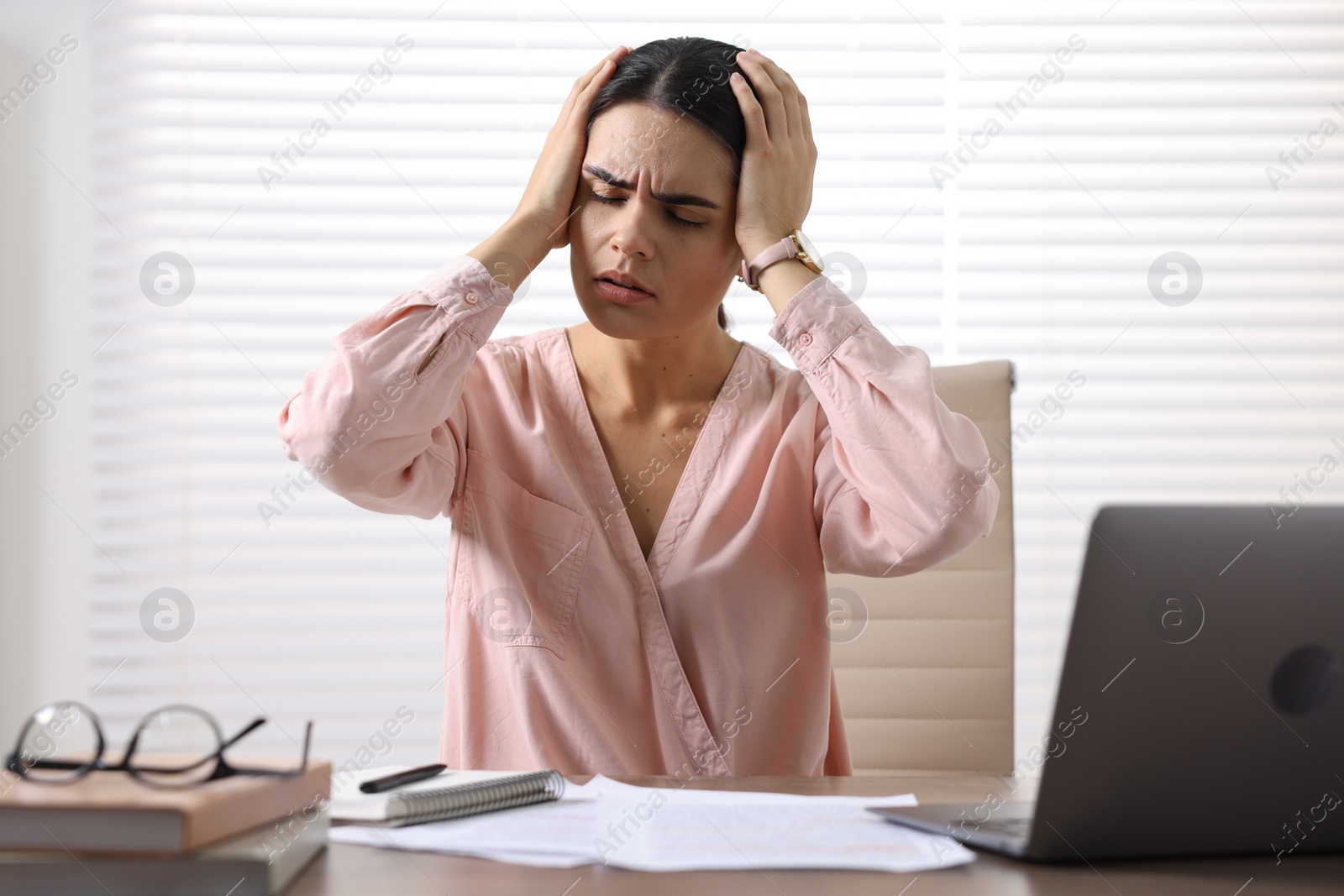 Photo of Young woman suffering from headache at wooden table in office