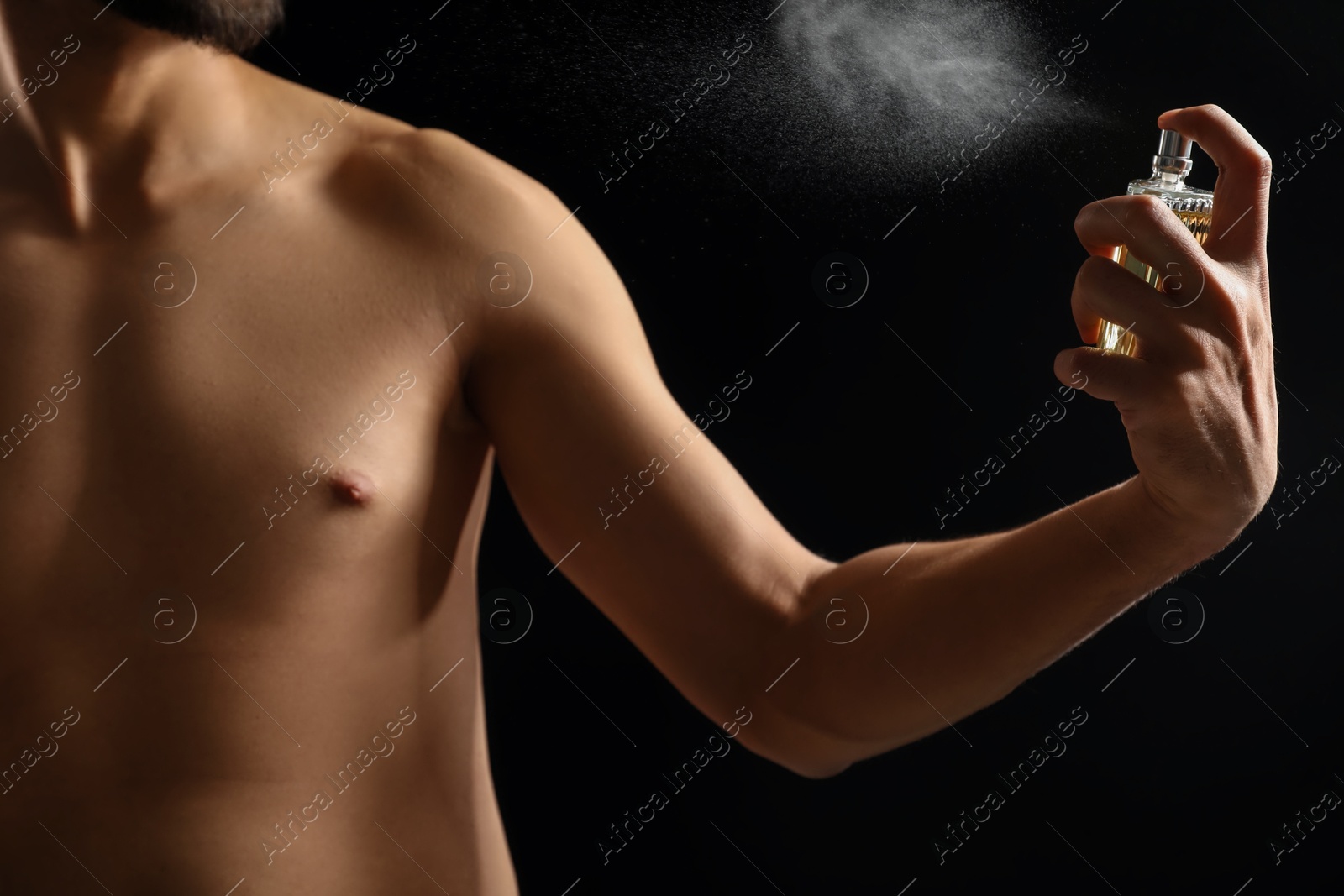 Photo of Man spraying luxury perfume on dark background, closeup