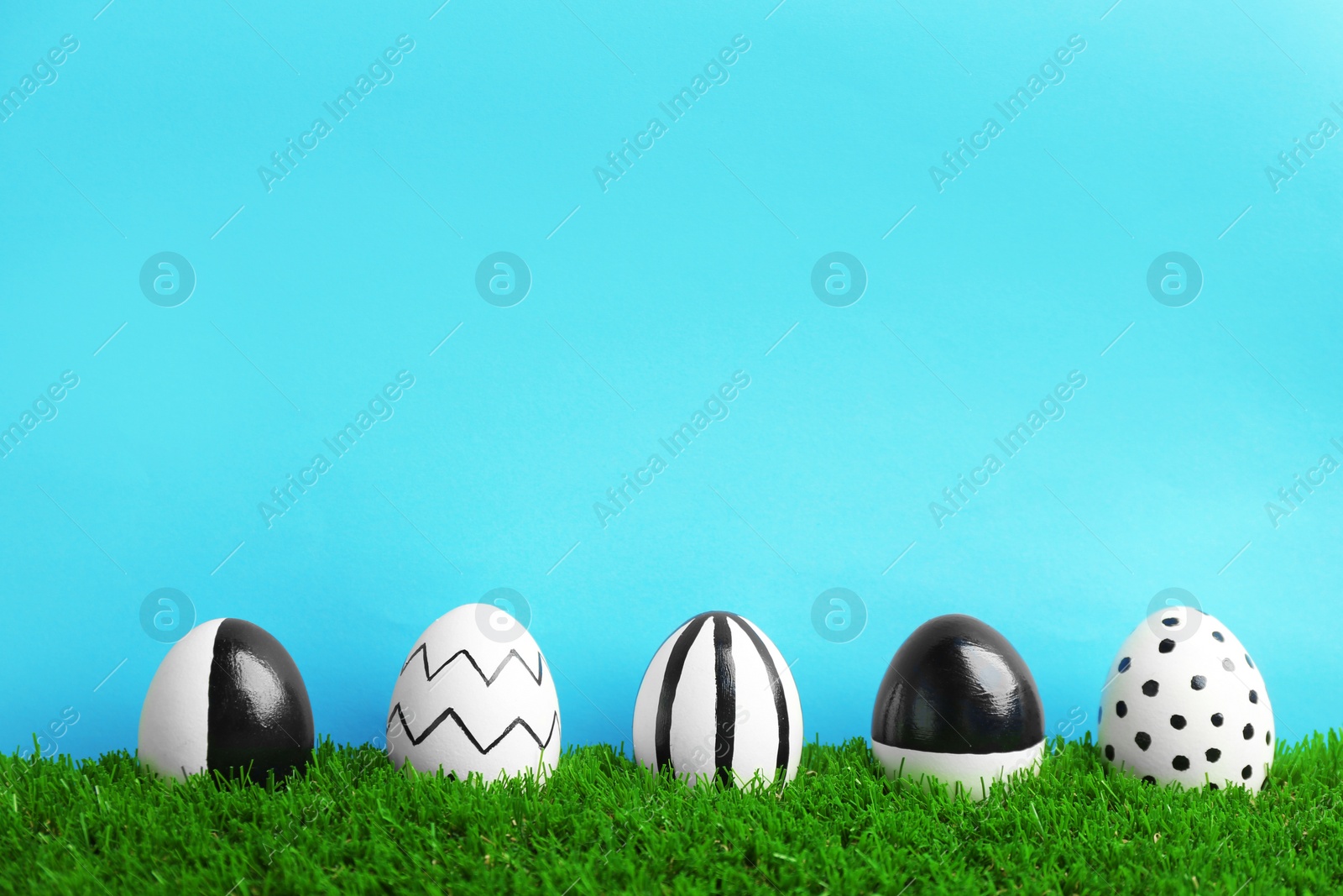 Photo of Line of painted Easter eggs on green lawn against color background, space for text