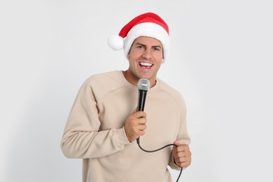 Photo of Happy man in Santa Claus hat singing with microphone on white background. Christmas music
