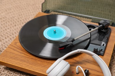Photo of Stylish turntable with vinyl disc and headphones on carpet at home, closeup