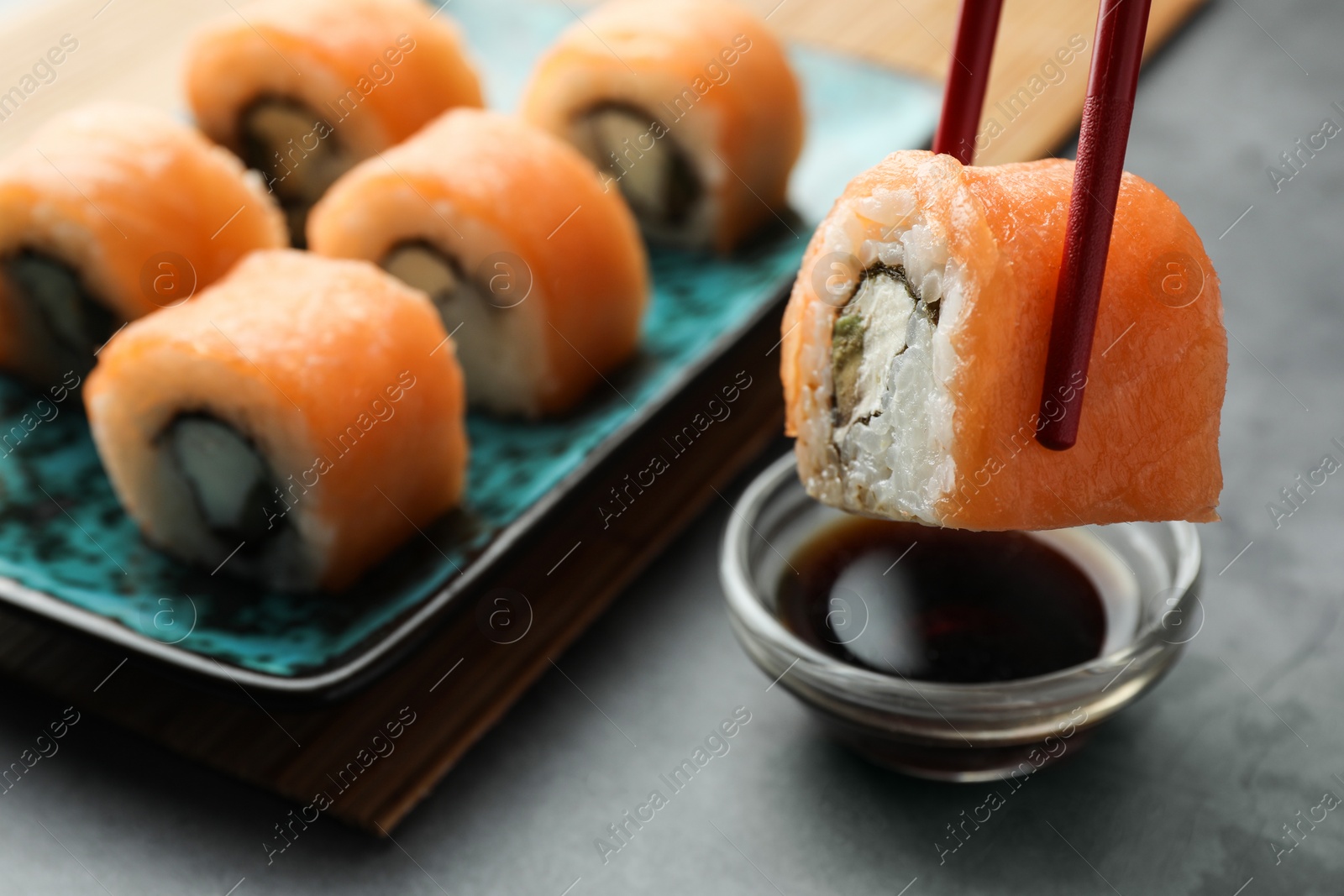 Photo of Dipping tasty sushi roll with salmon into soy sauce on grey table, closeup. Space for text