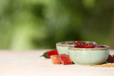 Photo of Tasty rhubarb sauce and ingredients on white table against blurred background, closeup. Space for text