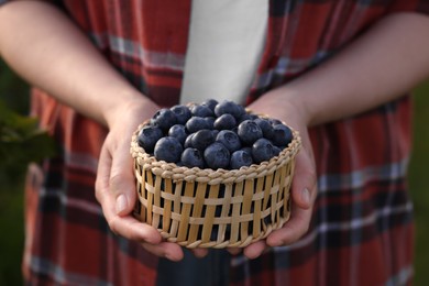 Photo of Woman with wicker bowl of wild blueberries, closeup. Seasonal berries