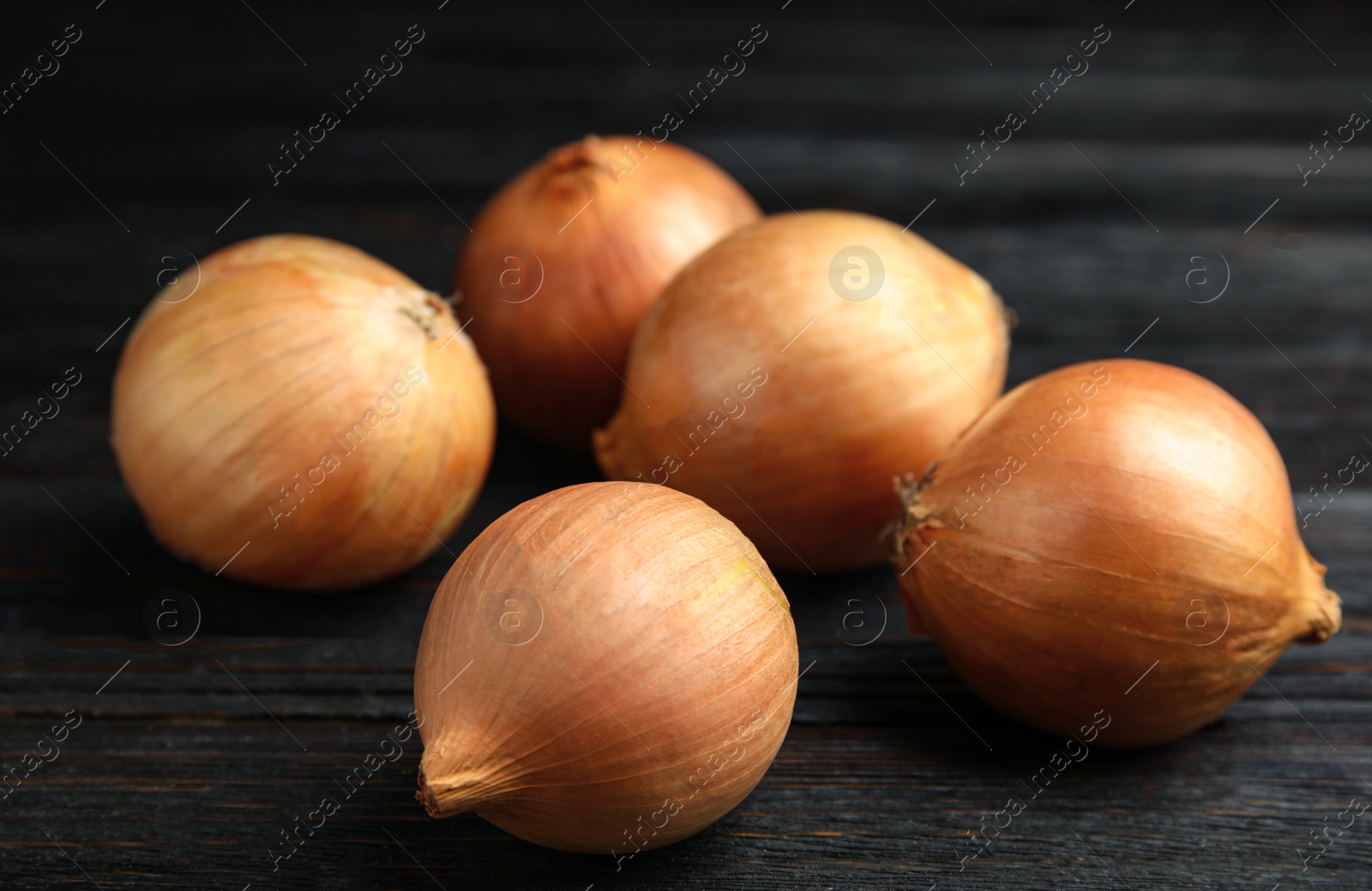 Photo of Ripe onions on black wooden table, closeup