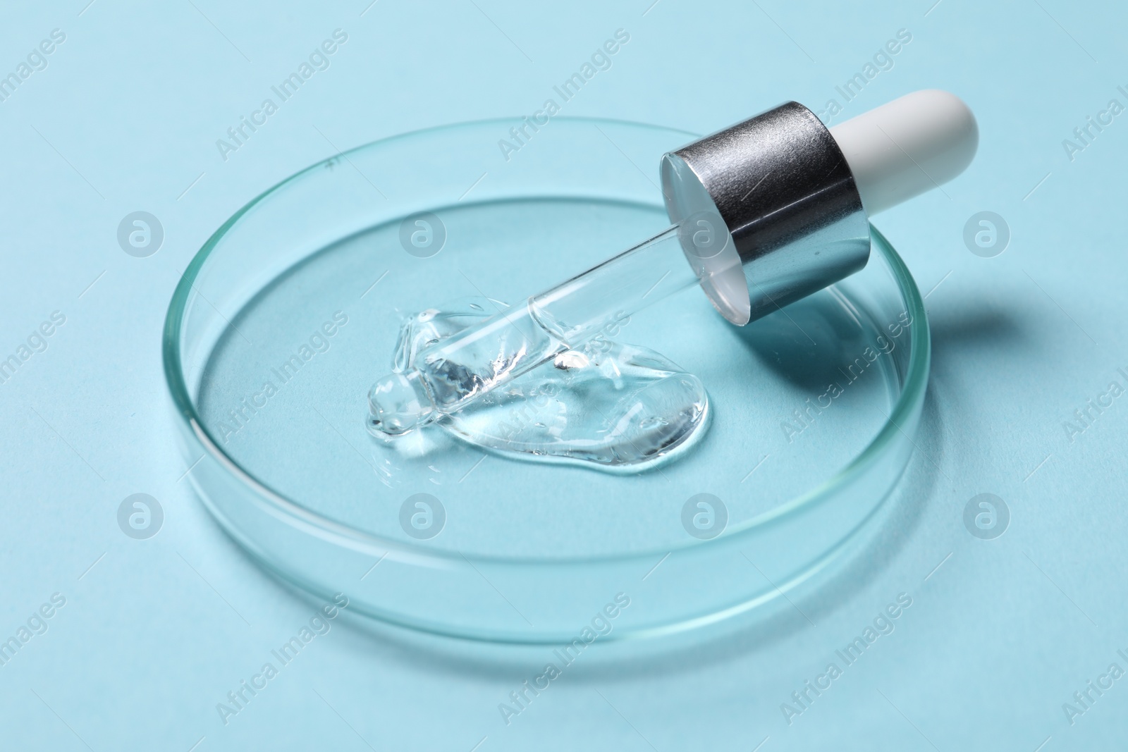 Photo of Petri dish with sample of cosmetic serum and pipette on light blue background, closeup