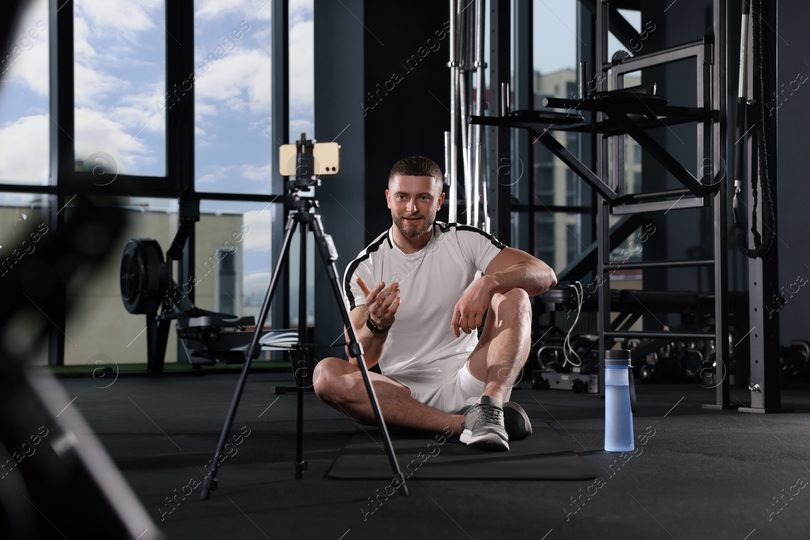 Photo of Trainer streaming online workout with phone at gym