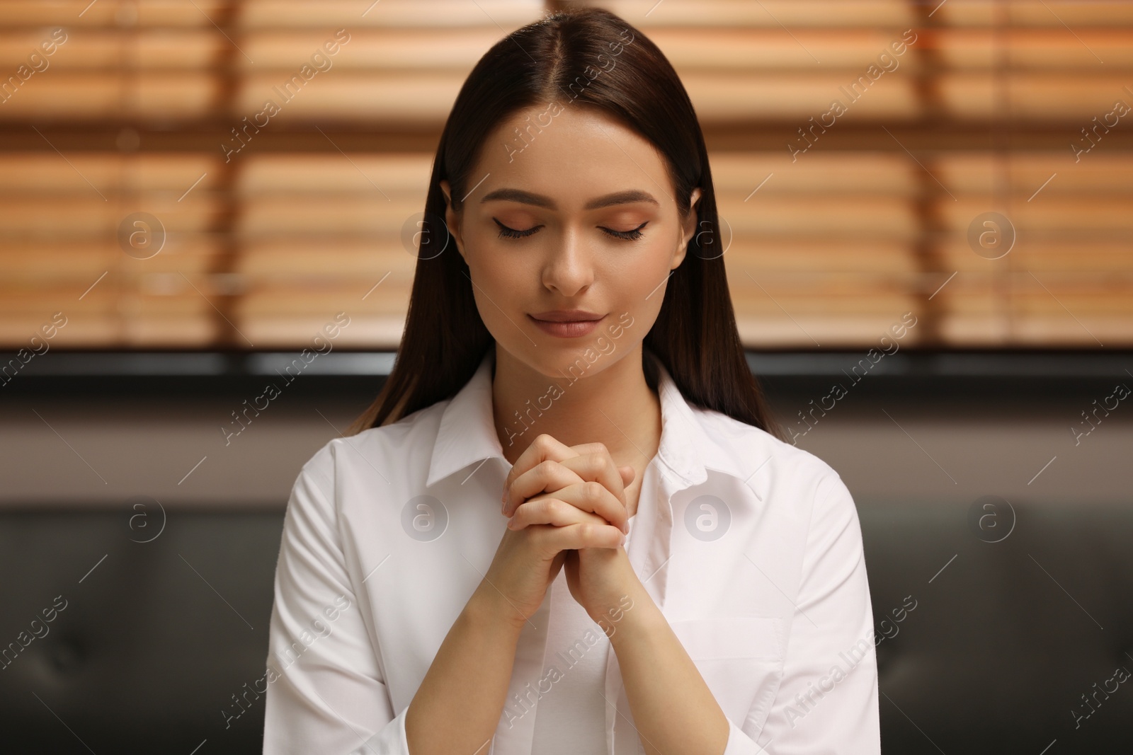 Photo of Religious young woman with clasped hands praying indoors