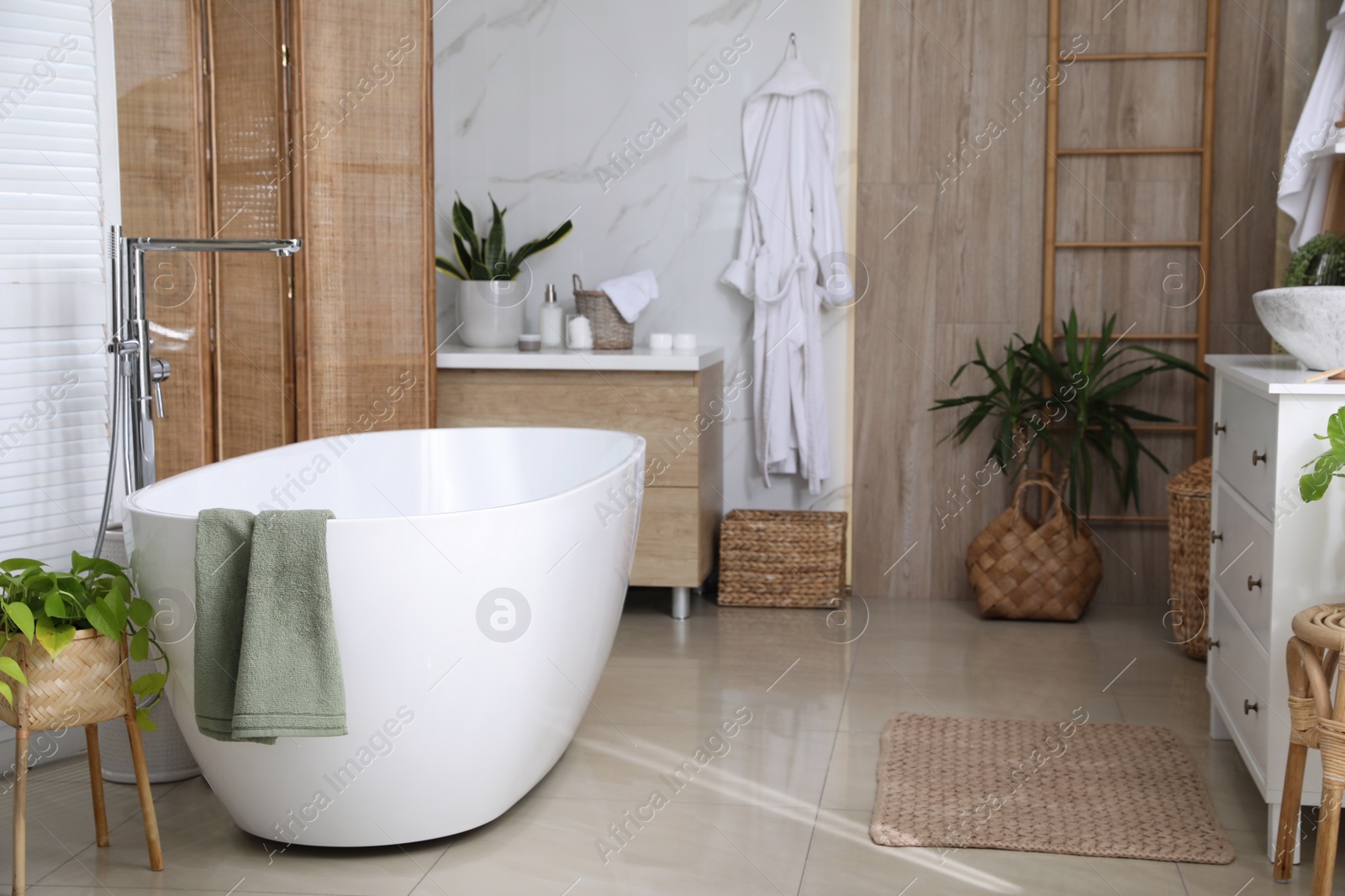 Photo of Modern white tub and beautiful green houseplants in bathroom. Interior design