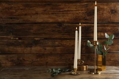Photo of Elegant candlesticks with burning candles and eucalyptus on wooden table. Space for text