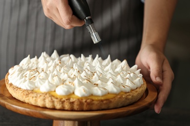 Photo of Woman toasting meringue on lemon pie with kitchen torch, closeup