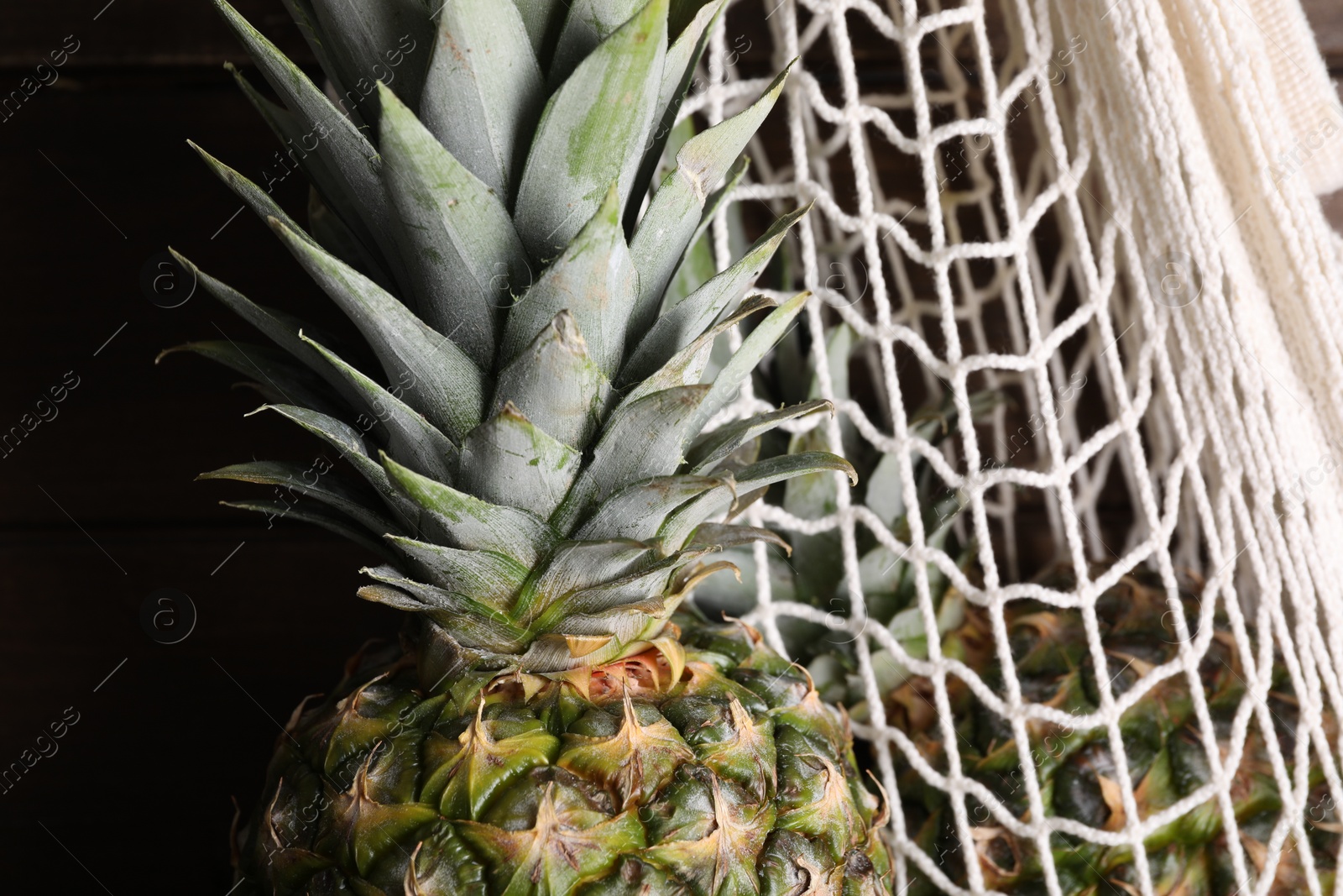 Photo of Whole ripe pineapples and net bag, closeup