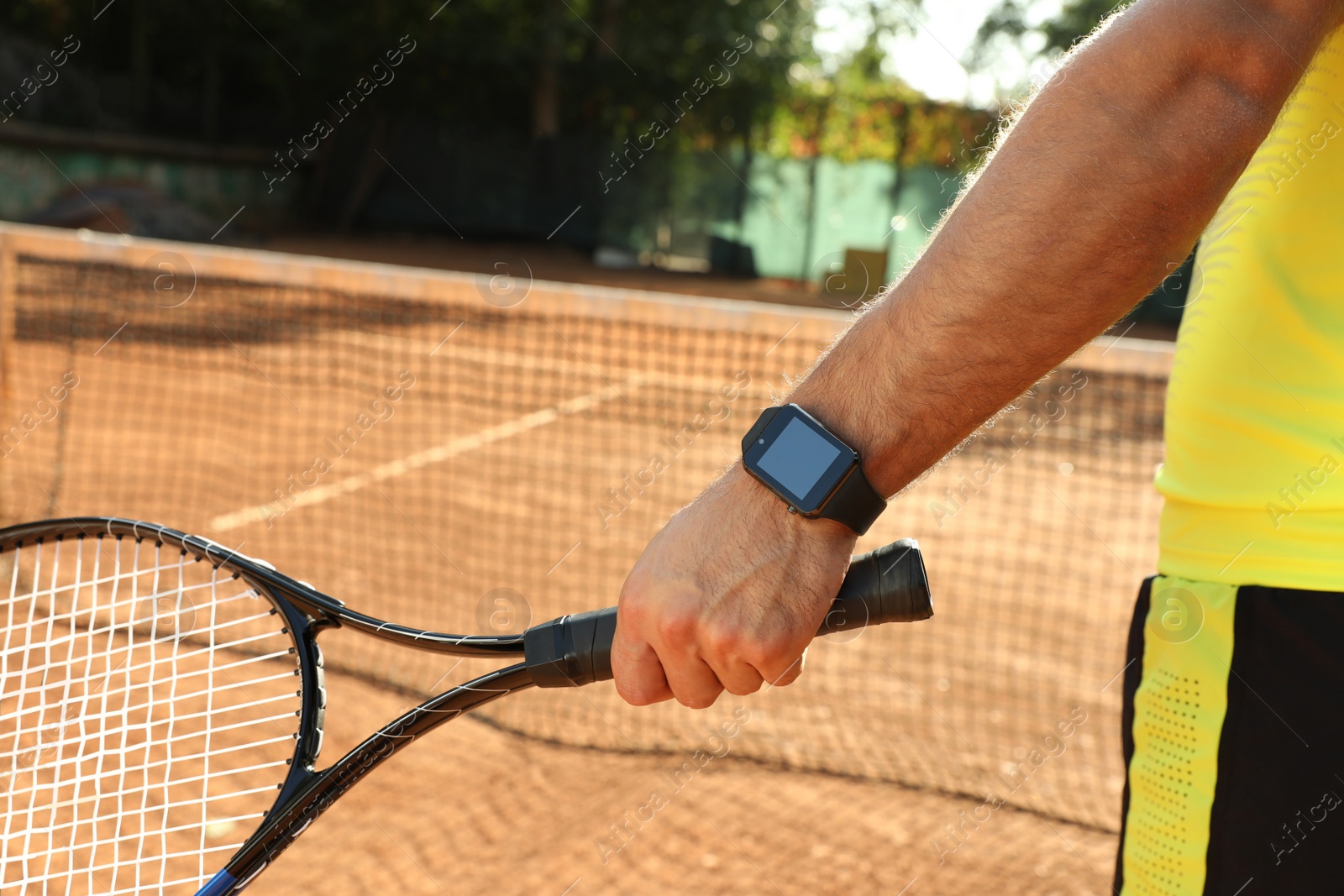 Photo of Man wearing modern smart watch during training on tennis court, closeup