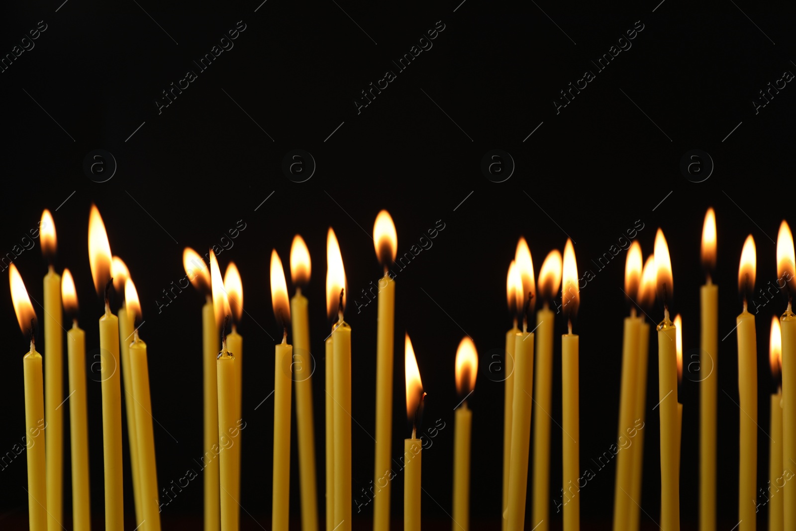 Photo of Many burning church candles on black background