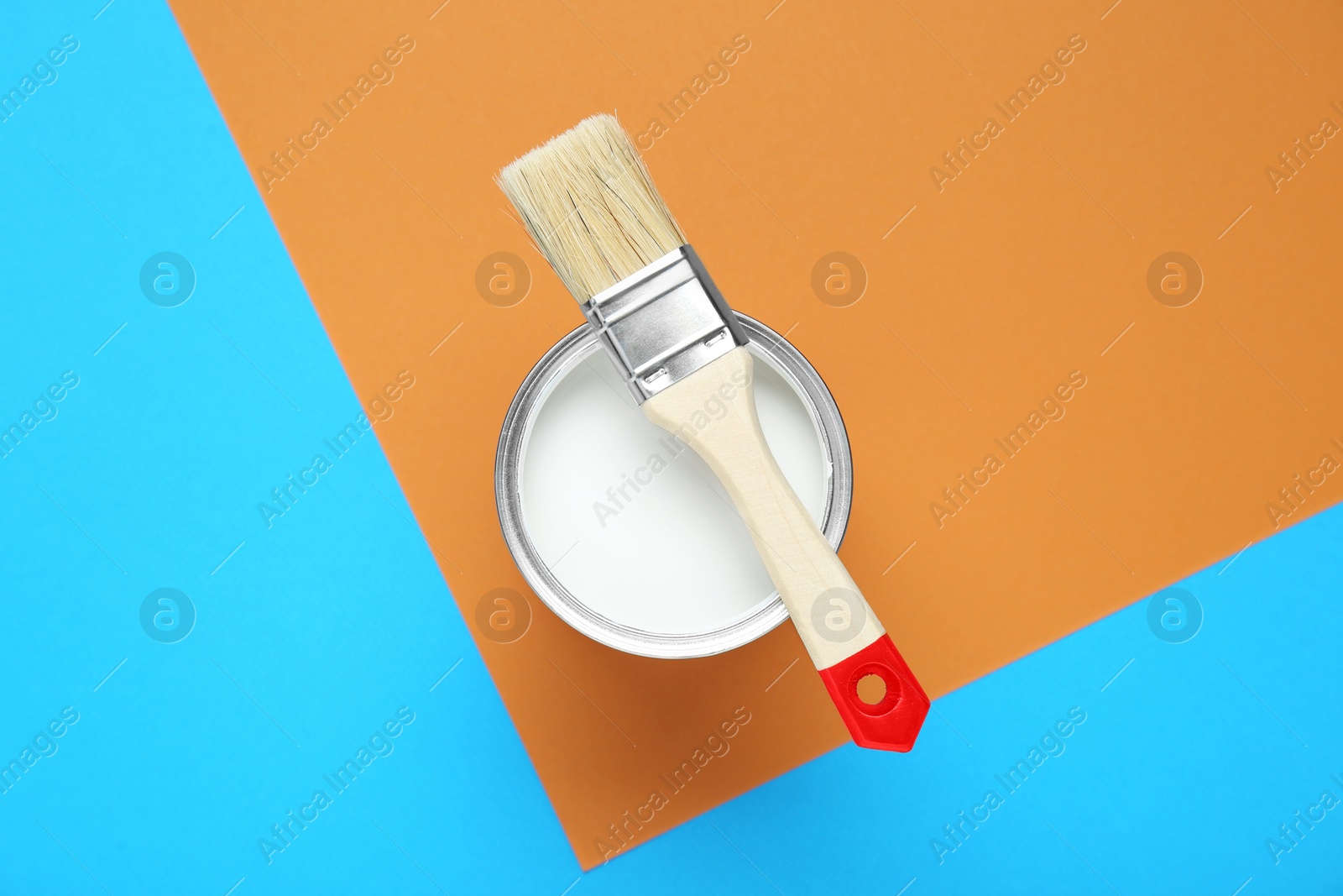 Photo of Can of white paint with brush on color background, top view