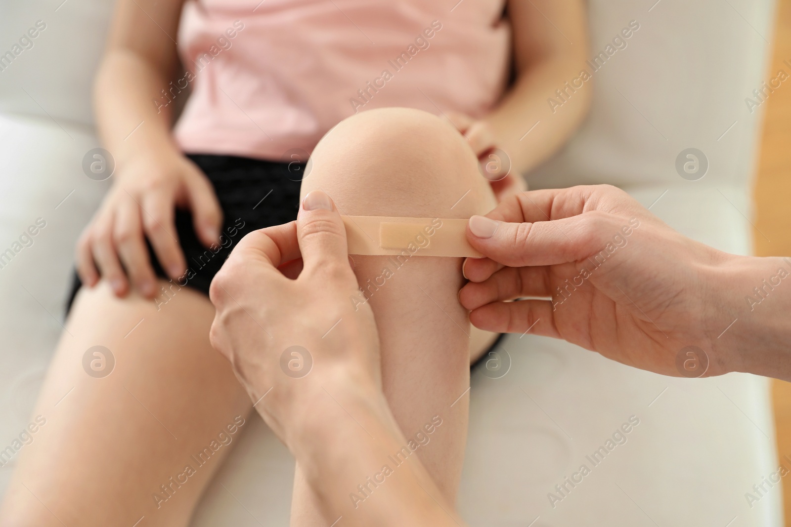 Photo of Doctor applying medical patch on little patient's injured knee indoors, closeup