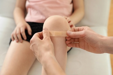 Photo of Doctor applying medical patch on little patient's injured knee indoors, closeup