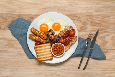 Plate with fried eggs, sausages, mushrooms, beans, bacon and toast on wooden table, flat lay. Traditional English breakfast