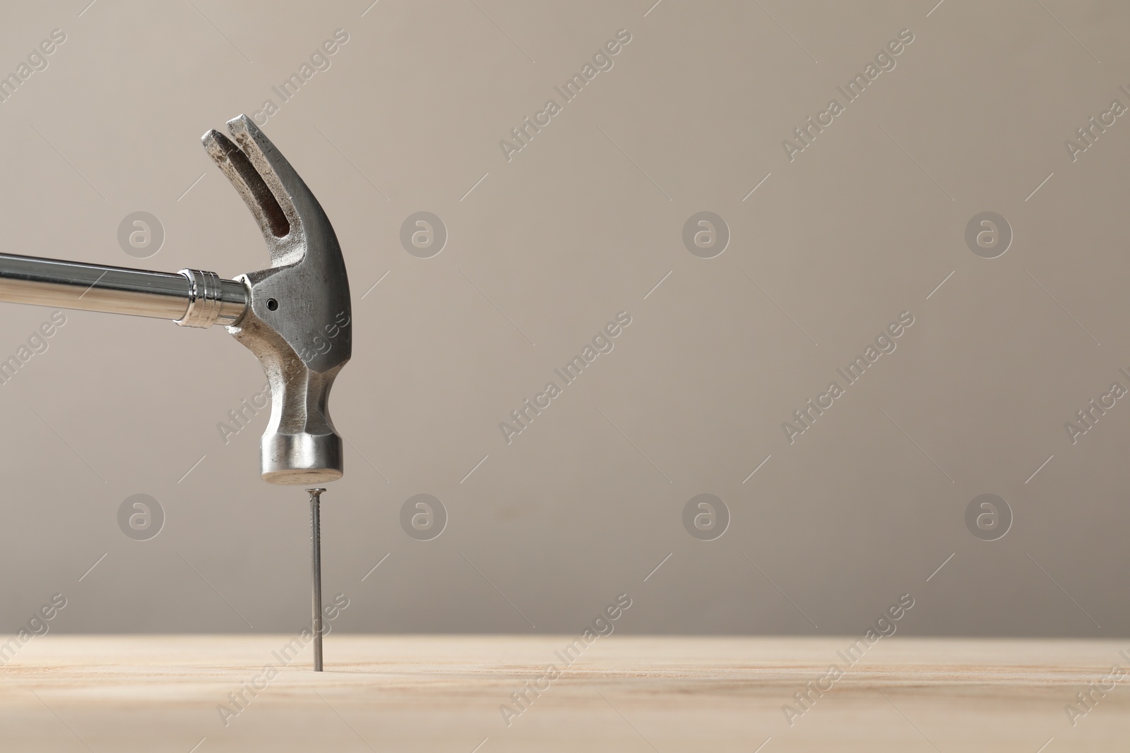 Photo of Hammering metal nail on wooden table against grey background. Space for text