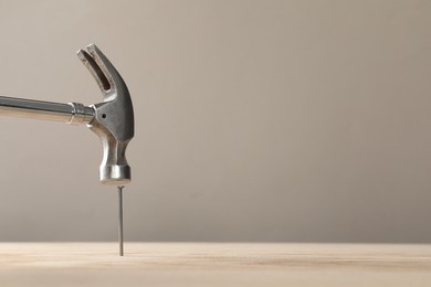 Hammering metal nail on wooden table against grey background. Space for text