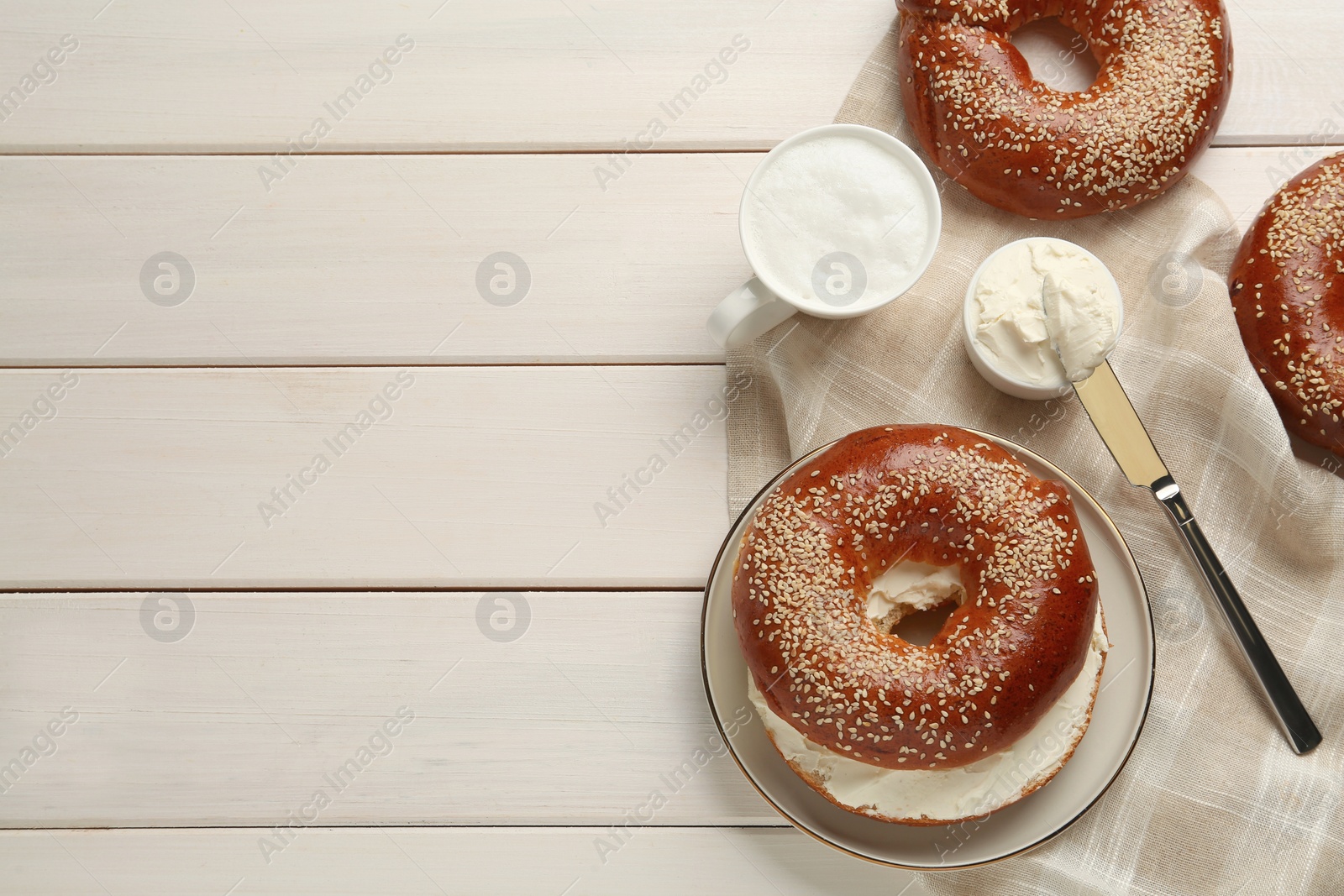 Photo of Delicious bagel with cream cheese and coffee on white wooden table, flat lay. Space for text