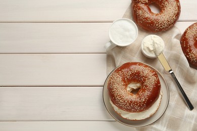 Photo of Delicious bagel with cream cheese and coffee on white wooden table, flat lay. Space for text