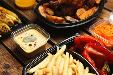 Plastic containers with different dishes on wooden table, closeup. Food delivery service