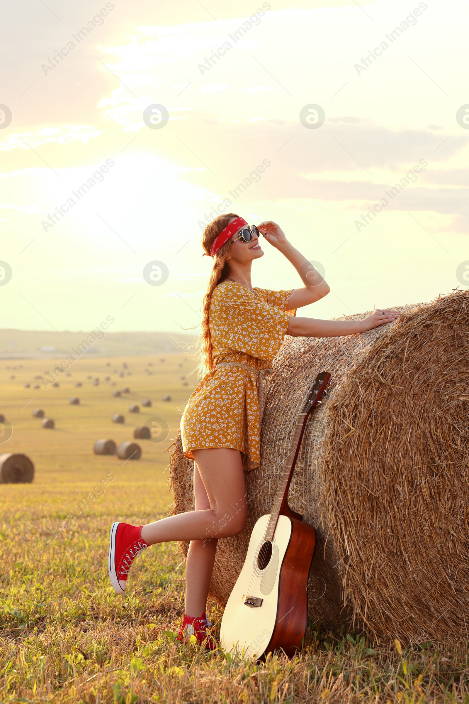 Photo of Happy hippie woman with guitar near hay bale in field, space for text