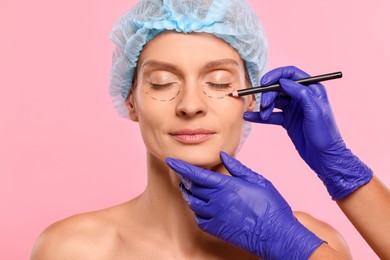 Photo of Doctor with pencil preparing patient for cosmetic surgery operation on pink background, closeup