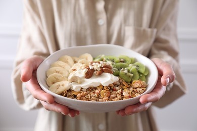 Photo of Woman holding bowl of tasty granola indoors, closeup