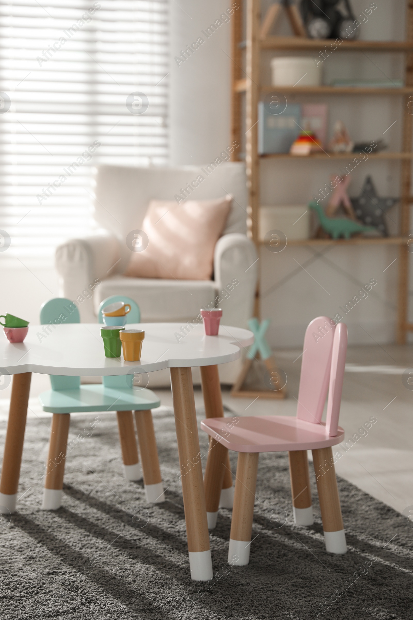 Photo of Small table and chairs with bunny ears in children's room interior