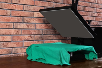 Heat press machine with t-shirt on wooden table near brick wall