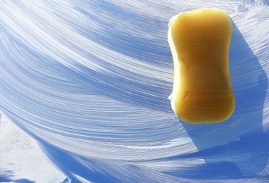 Photo of Sponge and cleaning foam on glass, closeup