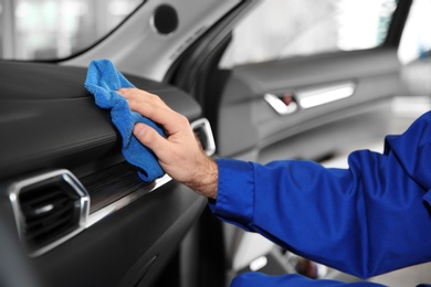 Worker cleaning automobile dashboard with rag at car wash, closeup