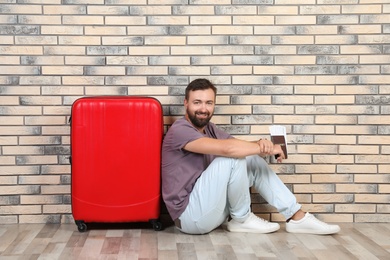 Photo of Man with suitcase and passport near brick wall. Vacation travel