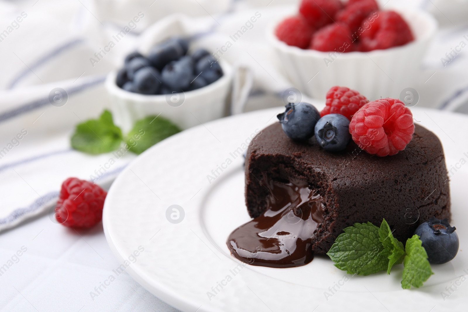 Photo of Plate with delicious chocolate fondant, berries and mint on white tiled table, closeup