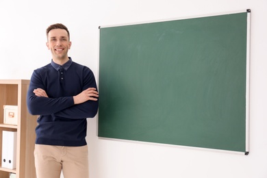 Photo of Young male teacher standing near blackboard in classroom