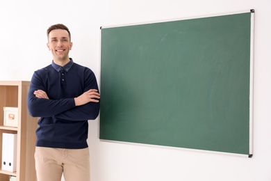 Young male teacher standing near blackboard in classroom