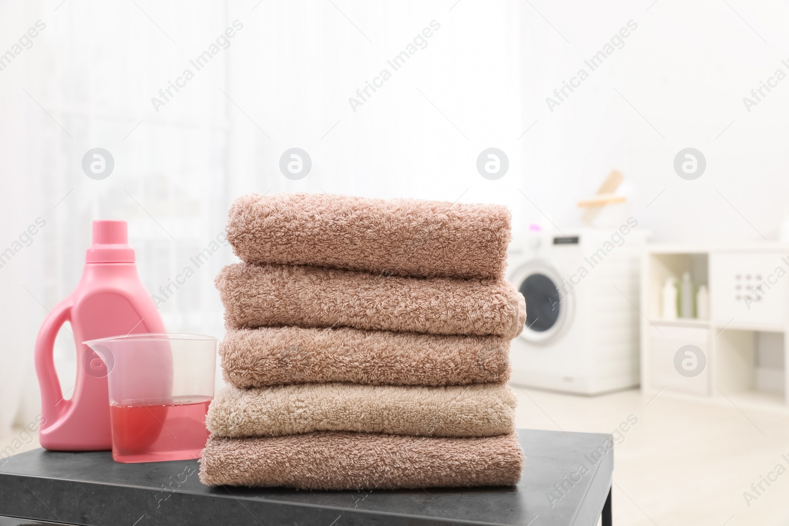 Photo of Stack of clean towels and liquid detergent on table in bathroom. Space for text