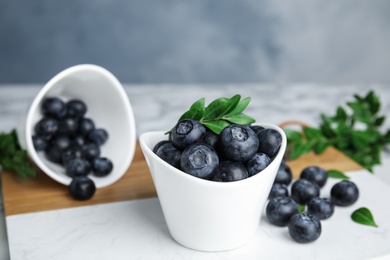 Photo of Bowls with tasty fresh blueberries and leaves on table