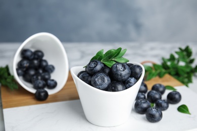 Bowls with tasty fresh blueberries and leaves on table