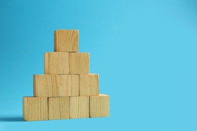 Photo of Pyramid of blank wooden cubes on light blue background, space for text